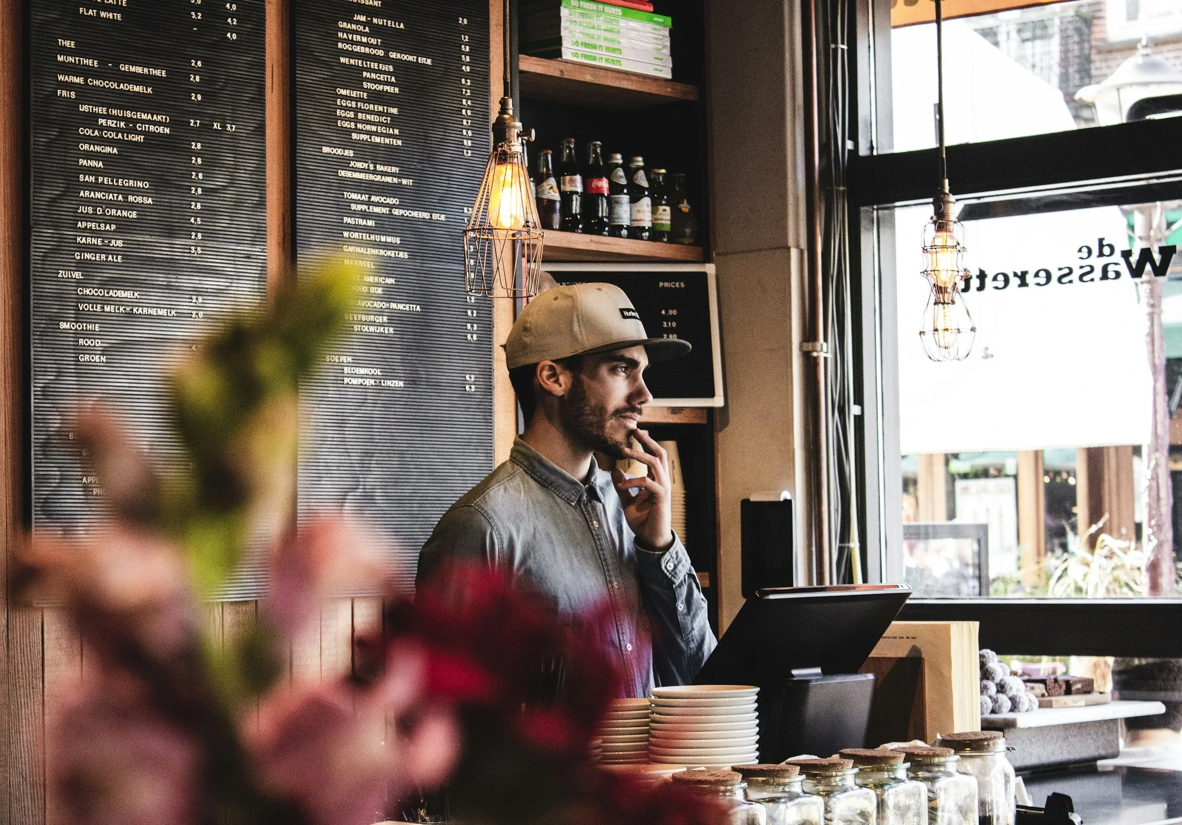 A cafe owner on the phone behind his counter, with the menu board behind him